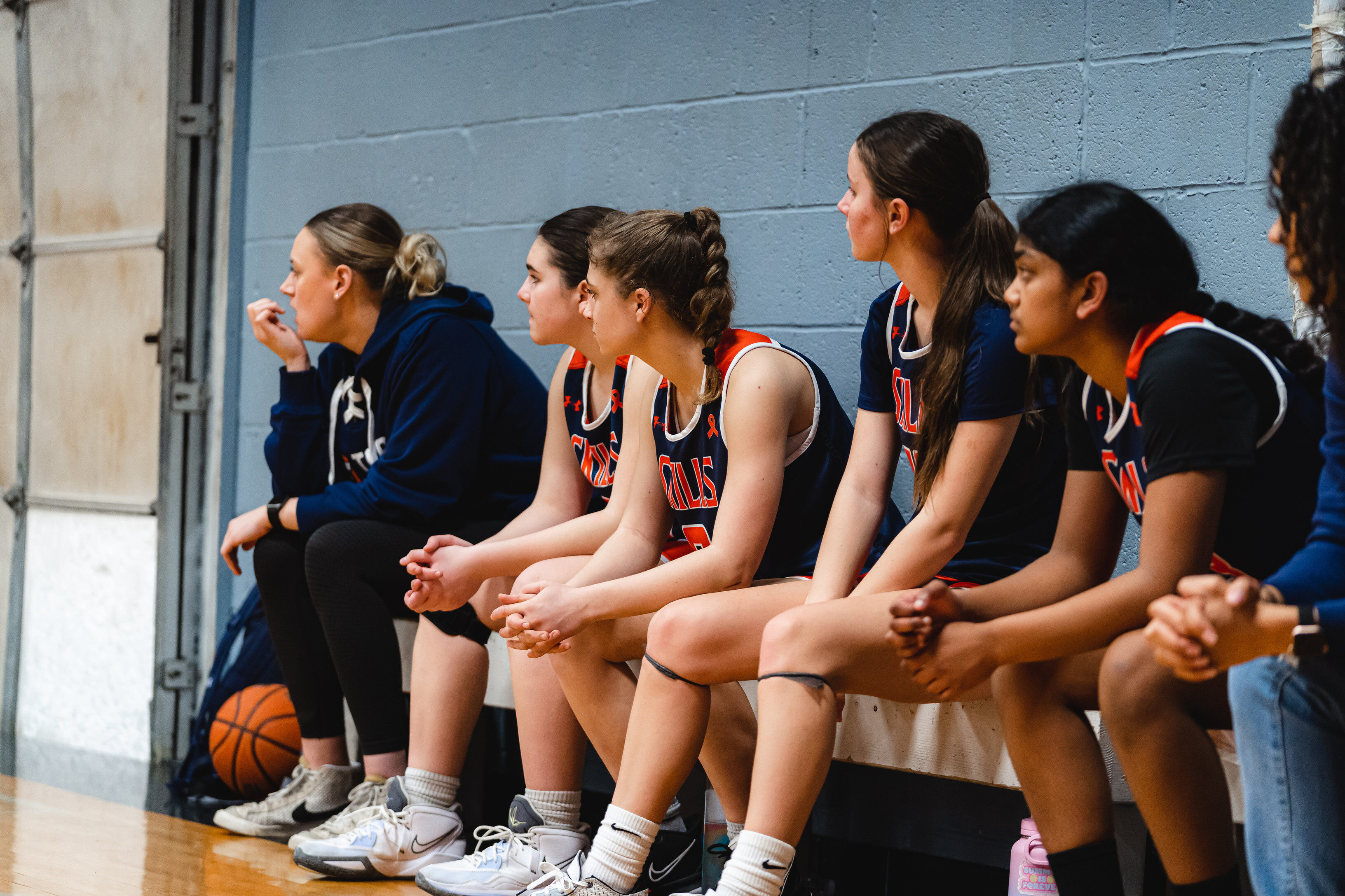 A youth basketball team sits on the bench watching the game