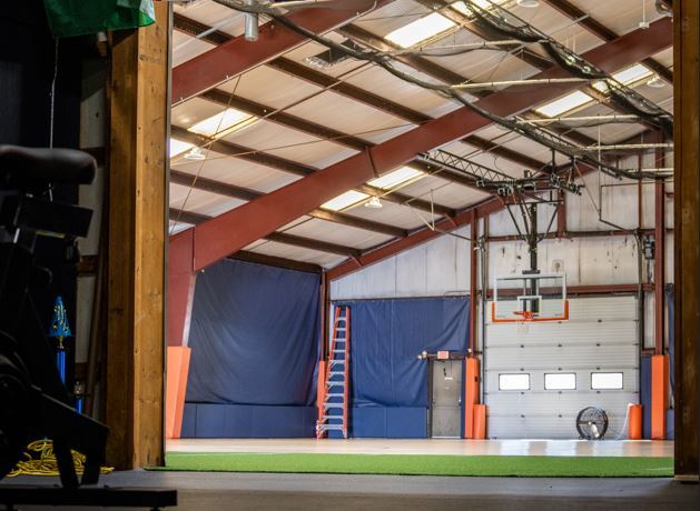 main facility view with baseball hoop, green turf and basketball floors, taken from dark weight room